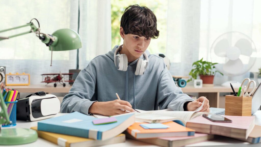 Autism in College: Challenges, Strengths, Support for Independence A student writing in a notebook surrounded by textbooks and study tools, illustrating the day-to-day life related to autism in college.