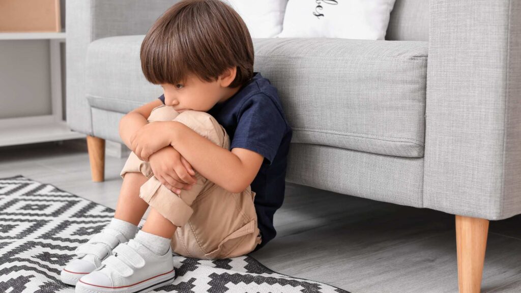 Level 1 Autism: Support Needs, Misconceptions, and What Families Should Know A young child with ASD sitting on the floor hugging their knees, showing a moment of sensory overwhelm