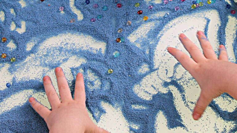 Autism and play represented by a young child's hands making patterns in blue sand.