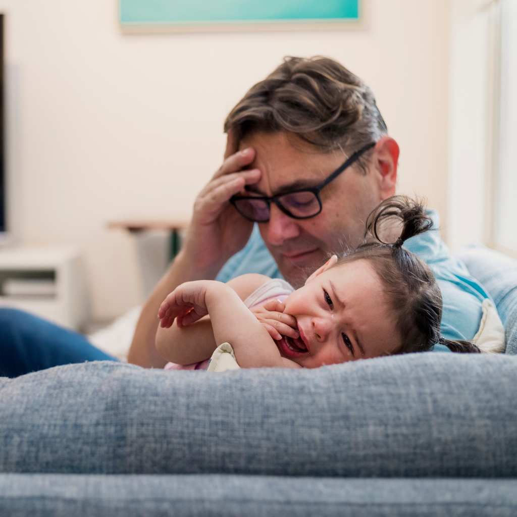 Father comforting a crying child on a sofa at home, showing stress linked to sensory sensitivities in autism.