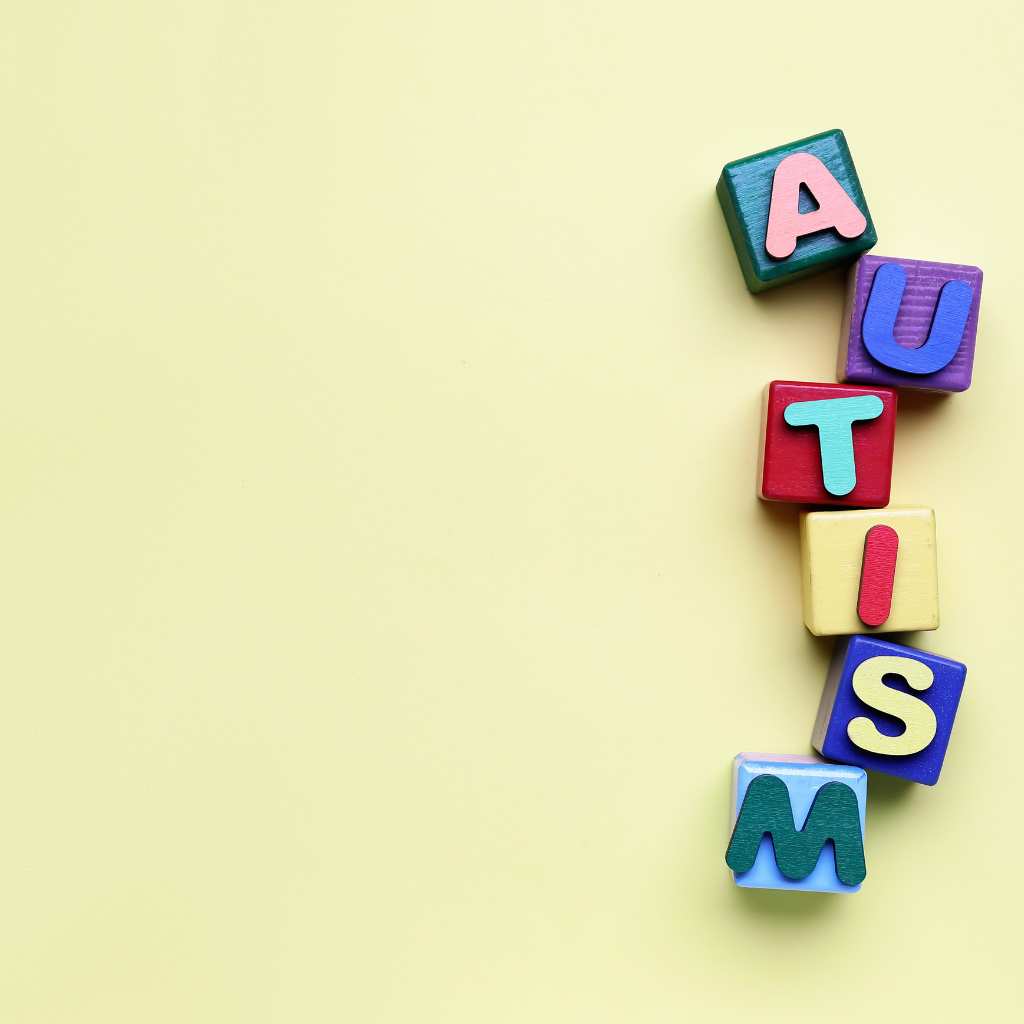 Letter blocks in different colors spelling autism on a plain grid-patterned yellow surface