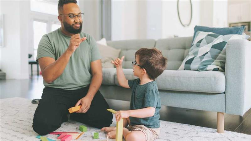Therapist and young boy using hand signs to communicate during play therapy, illustrating minimally verbal autism and alternative communication methods.