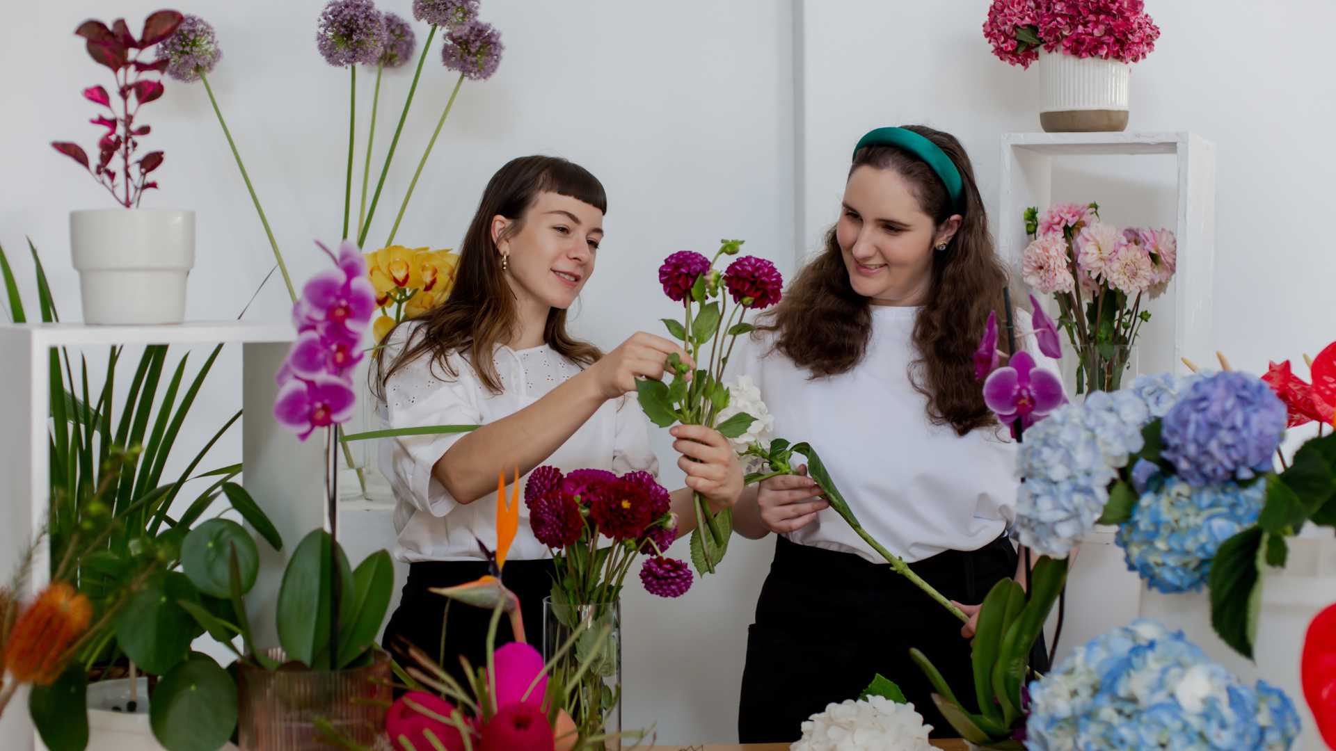Two women arranging colorful flowers together, representing collaboration, inclusion, and the shift from the medical model to the social model of understanding neurodiversity and neurodivergent perspectives