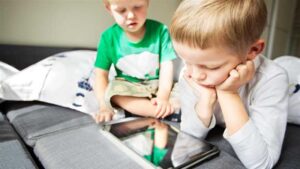 Two young children sitting on a couch using a tablet, representing nonverbal autism and alternative communication through visual aids.