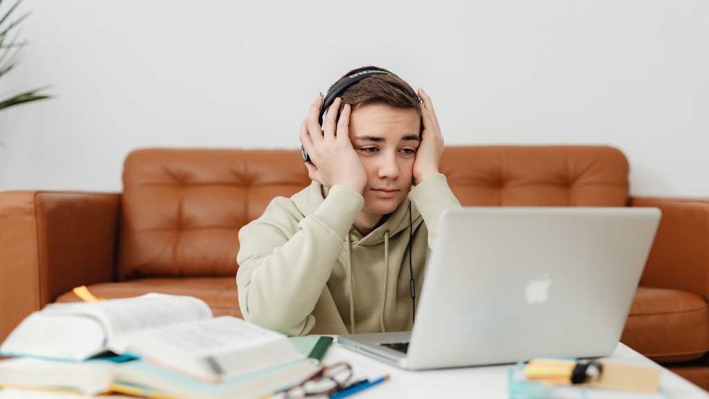 Young adult wearing headphones and studying on a laptop, representing the challenges and ongoing support needed to improve quality of life for adults with autism.