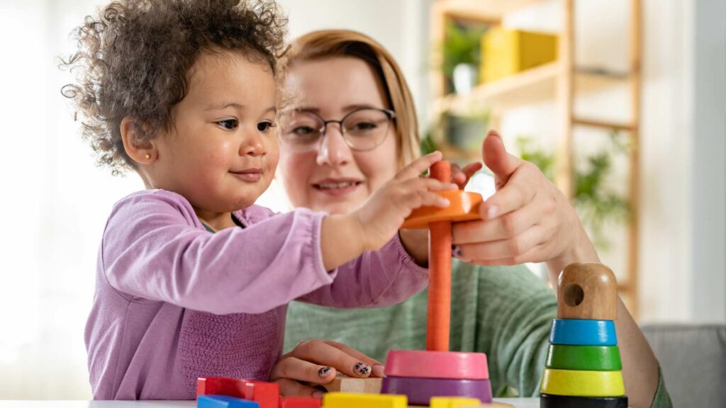 Caregiver supporting a toddler during a play-based ABA therapy activity