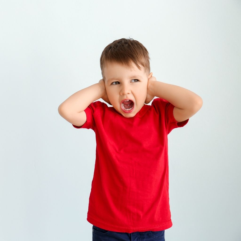Child living with autism covering his ears in response to sensory input